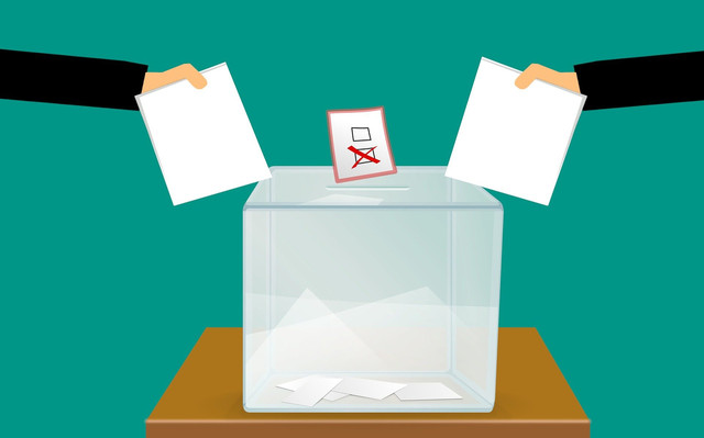 Zwei (unsichtbare) Personen stecken jeweils einen Wahlzettel in die dafür vorgesehene Urne.