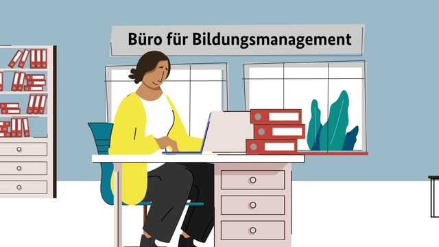 Eine Frau sitzt an einem Schreibtisch im Bildungsbüro, vor sich mehrere Aktenordner gestapelt.