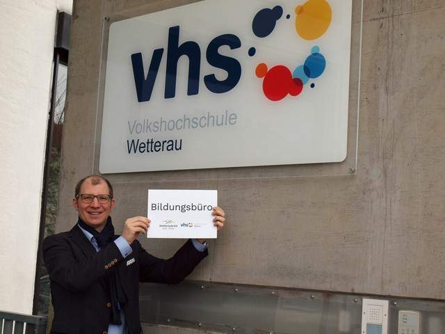 Landrat hält das Schild des neuen Bildungsbüros hoch