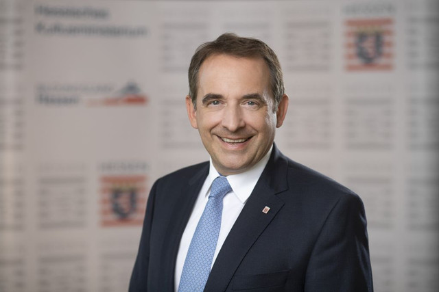 Amtsträger der hessischen Landesregierung in Anzug und Krawatte vor dem HIntergrund des Hessenwappens