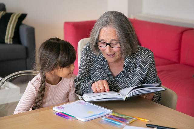 Seniorin liest gemeinsam mit einem Mädchen im Grundschulalter ein Buch.