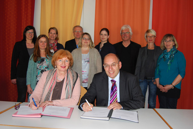 Bildmitte, sitzend: Umringt von Mitgliedern der Steuerungsgruppe des Bildungsforums Baunatal unterzeichnen Felicitas von Küchler (INBAS GmbH) und Bürgermeister Manfred Schaub die Kooperationsvereinbarung. Foto: Stadt Baunatal